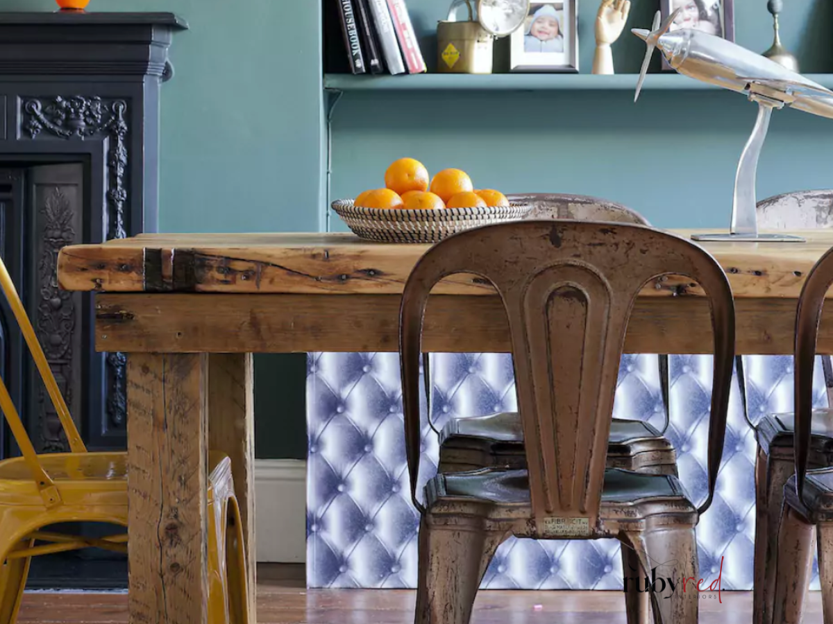 1 Rustic farmhouse dining area with reclaimed wooden table, vintage metal chairs, teal walls, and traditional fireplace — cosy farmhouse interior design inspiration.